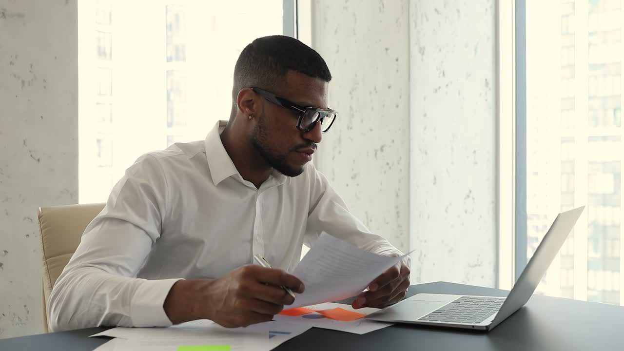 African businessman sit at workplace desk use laptop, examining document