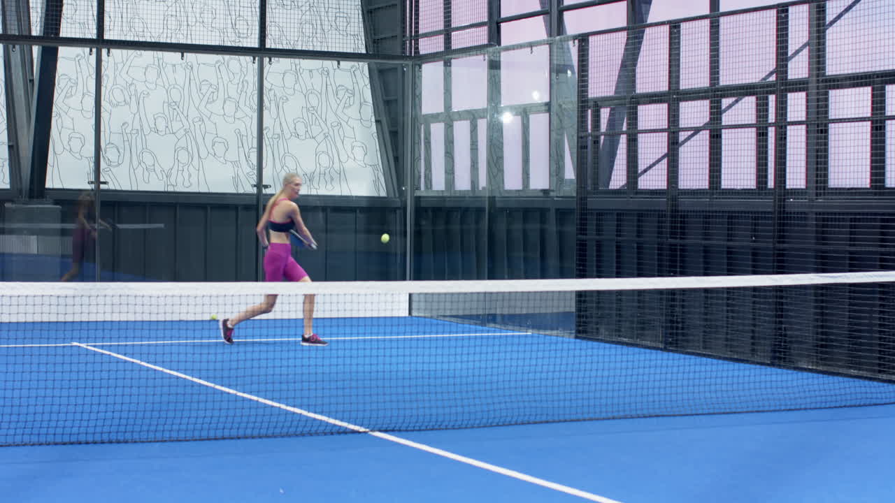 Woman playing padel tennis on blue indoor court, hitting ball with racket
