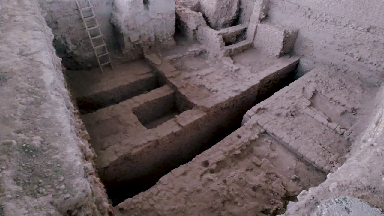 Excavación arqueológica en la India que muestra profundas zanjas, cimientos de ladrillo antiguos, acceso con escalera y estructuras preservadas que se utilizan para la investigación del patrimonio, la enseñanza de la historia y el contenido de los museos.