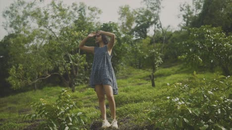 Ganzkörperfrau-Hebt-Hände,-Um-Haare-Zu-Reparieren,-Während-Sie-Im-Obstgarten-Mit-Grasbewachsenem-Hügel-Steht