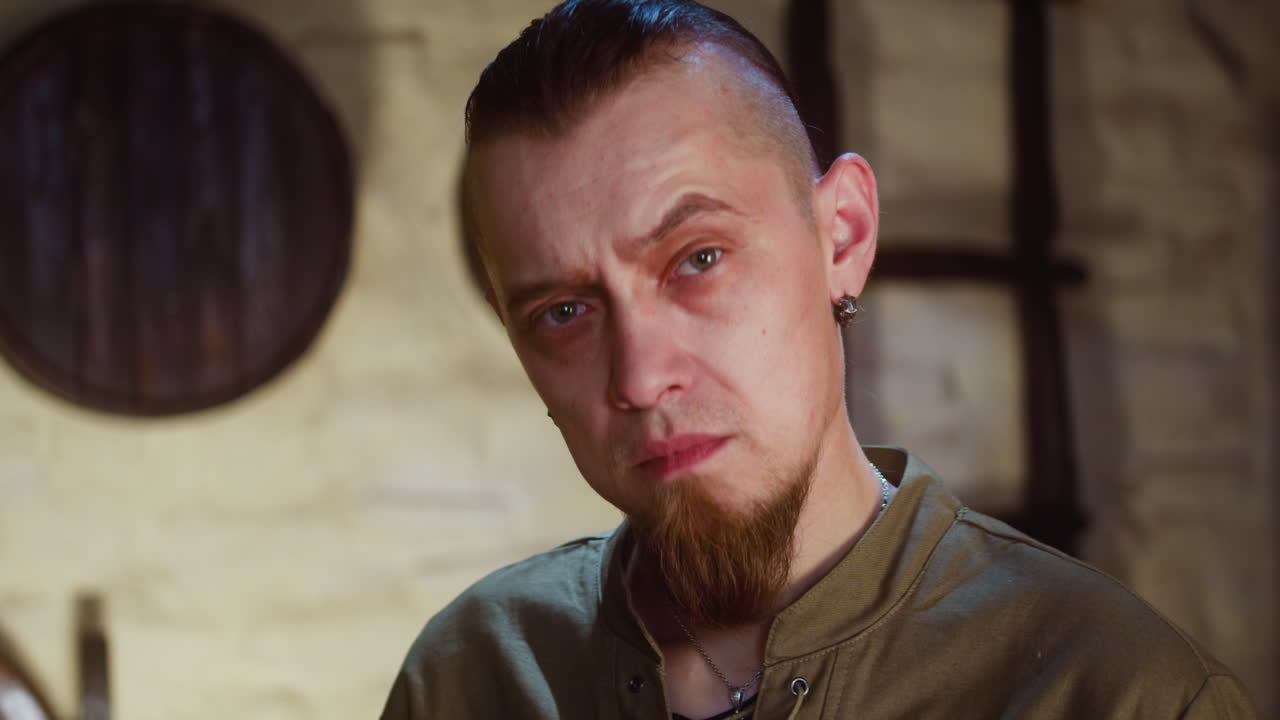 вдумчивый человек в средневековой таверне крупным планом. сомнительный гость с бородой поднимает брови, принимая решение в пабе. историческая реконструкция и ролевая игра