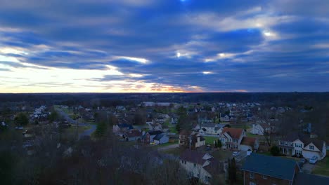 Rising-above-the-winter-trees,-displaying-a-suburban-neighborhood-and-a-beautiful-sunset