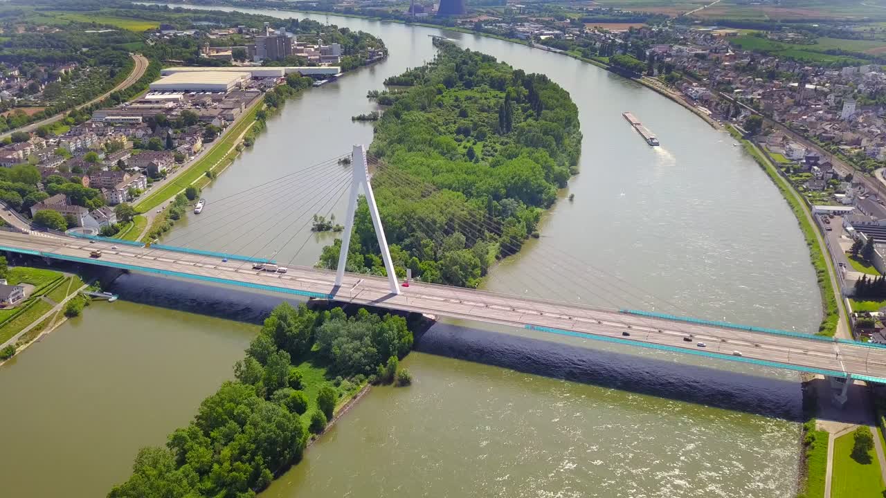 A breathtaking aerial view of the Neuwied Rhine Bridge, capturing busy road traffic as trucks and cars cross ovver the river. A key European trade corridor, framed by lush nature and urban landscape.