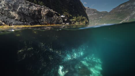 a large boulder rests at the shore of geiranger fjord, with its underwater half revealed by the crystal-clear water