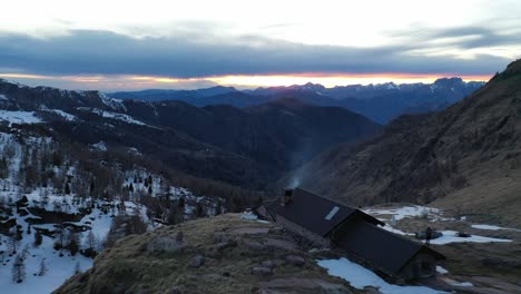 Dron-Sobre-La-Cabaña-De-Montaña-Bivacco-Marino-Bassi-Con-Una-Vista-épica-Del-Atardecer-Hacia-El-Valle