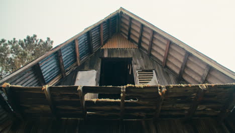 Abandoned-zinc-roofed-triangle-log-cabin-with-caribbean-pine-trees-in-the-mountains-and-cloudy-sky