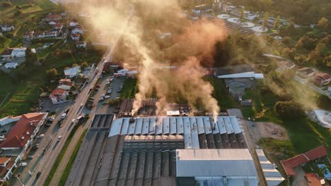 Aerial - large industrial factory releasing smoke into the air during sunset.