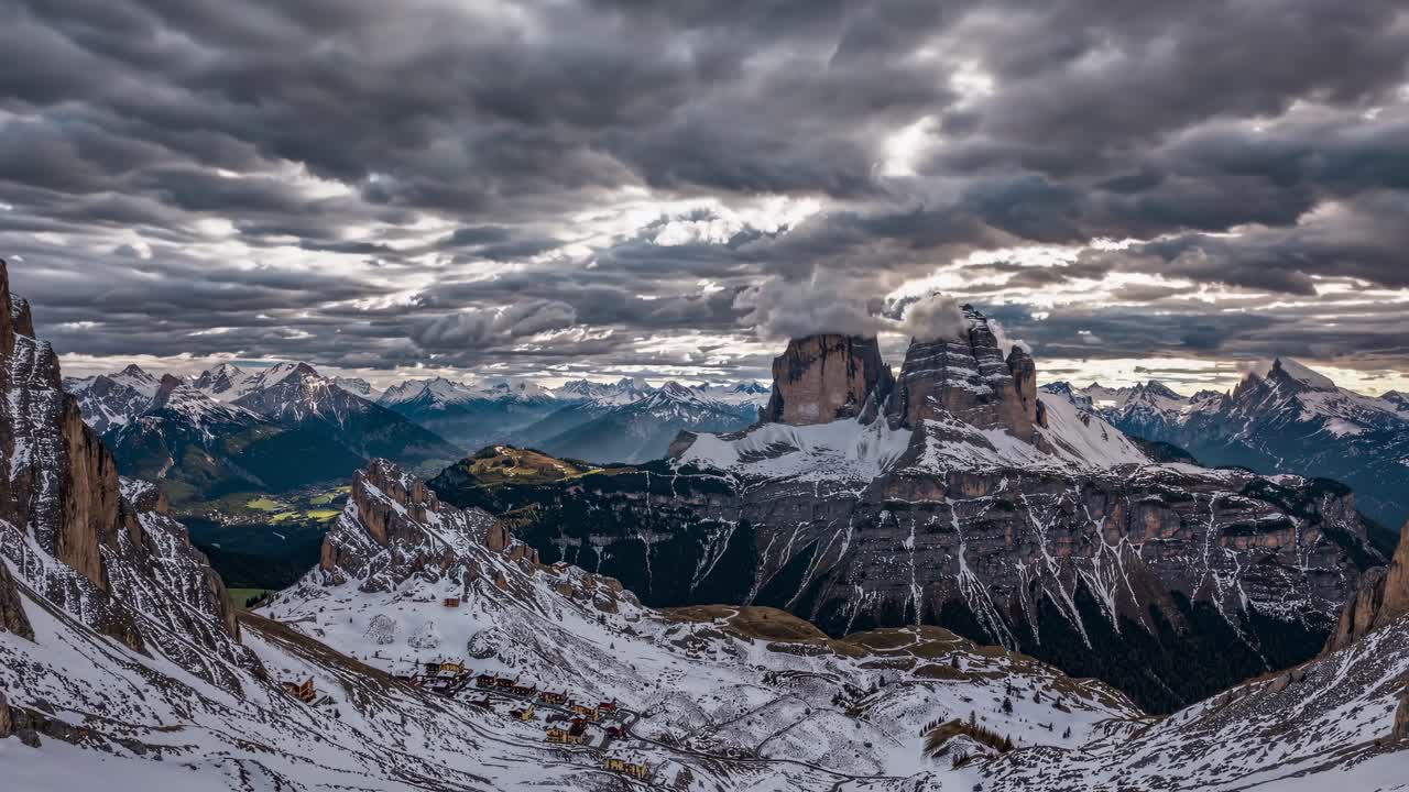 Aerial video shot of snow-capped mountains under dramatic clouds, showcasing rugged peaks and vast