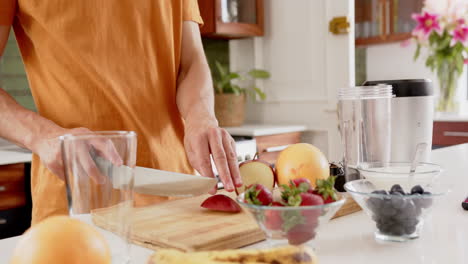 midsection of biracial man chopping fruit for healthy smoothie in kitchen, copy space, slow motion