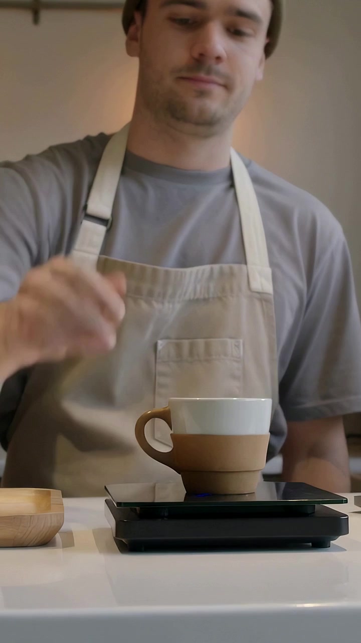 Video verticale: Inquadratura di una tazza bicolore, barista con grembiule che posiziona la tazza su una bilancia per pesare in un caffè