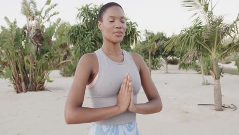 Relaxed-biracial-woman-practicing-yoga,-meditating-on-beach,-slow-motion