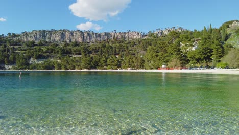 a view of the crystal-clear water, reflecting nature's epic beauty, the stunning panorama includes magnificent mountains and lush greenery, all residing beneath a radiant blue sky