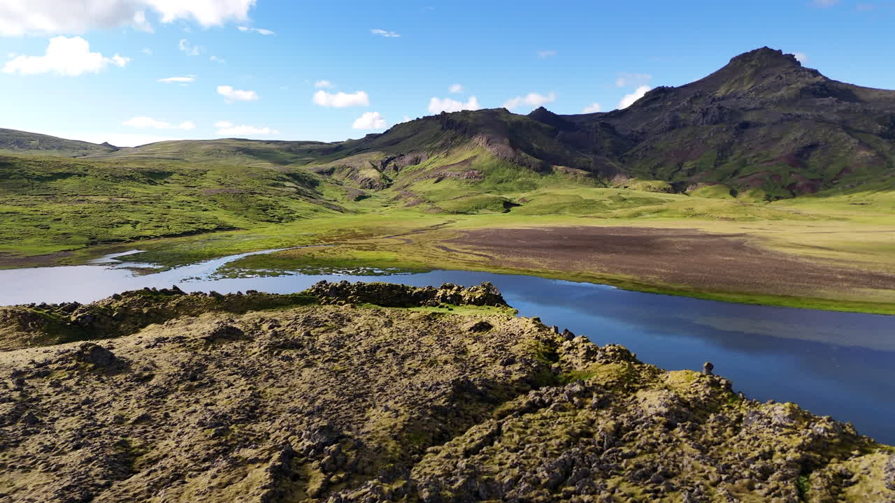 Aerial view of Selvallafoss and Selvallavatn on the Snæfellsnes Peninsula showing calm lake water mossy lava fields and distant mountains under bright clouds in a pristine Icelandic volcanic landscape