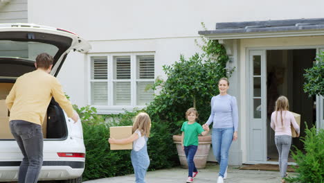 familia fuera de su nueva casa en el día de la mudanza descargando cajas del coche