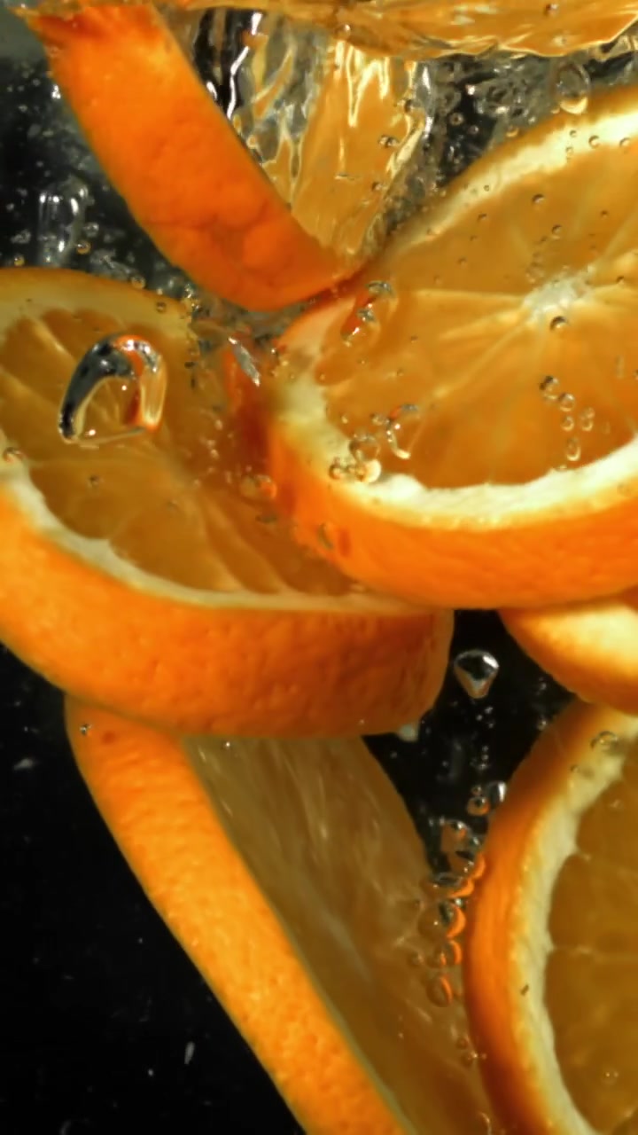 Fette d'arancia che cadono nell'acqua con bolle al rallentatore