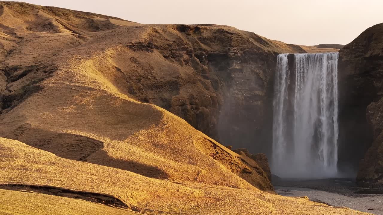 Majestic Skógafoss waterfall in Iceland, surrounded by golden hills and river