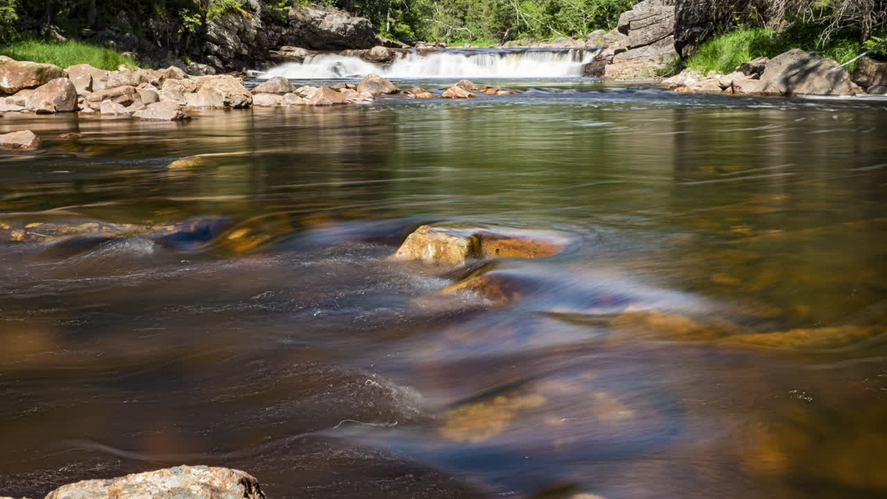 lapso de tiempo de río poco profundo que fluye rápidamente pequeña cascada en segundo plano.