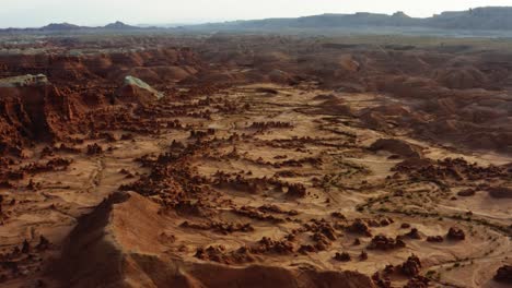 Gorgeous-dolly-in-aerial-drone-shot-of-the-beautiful-Goblin-Valley-Utah-State-Park-with-small-strange-mushroom-rock-formations-below-and-large-red-and-white-Butte's-in-the-background