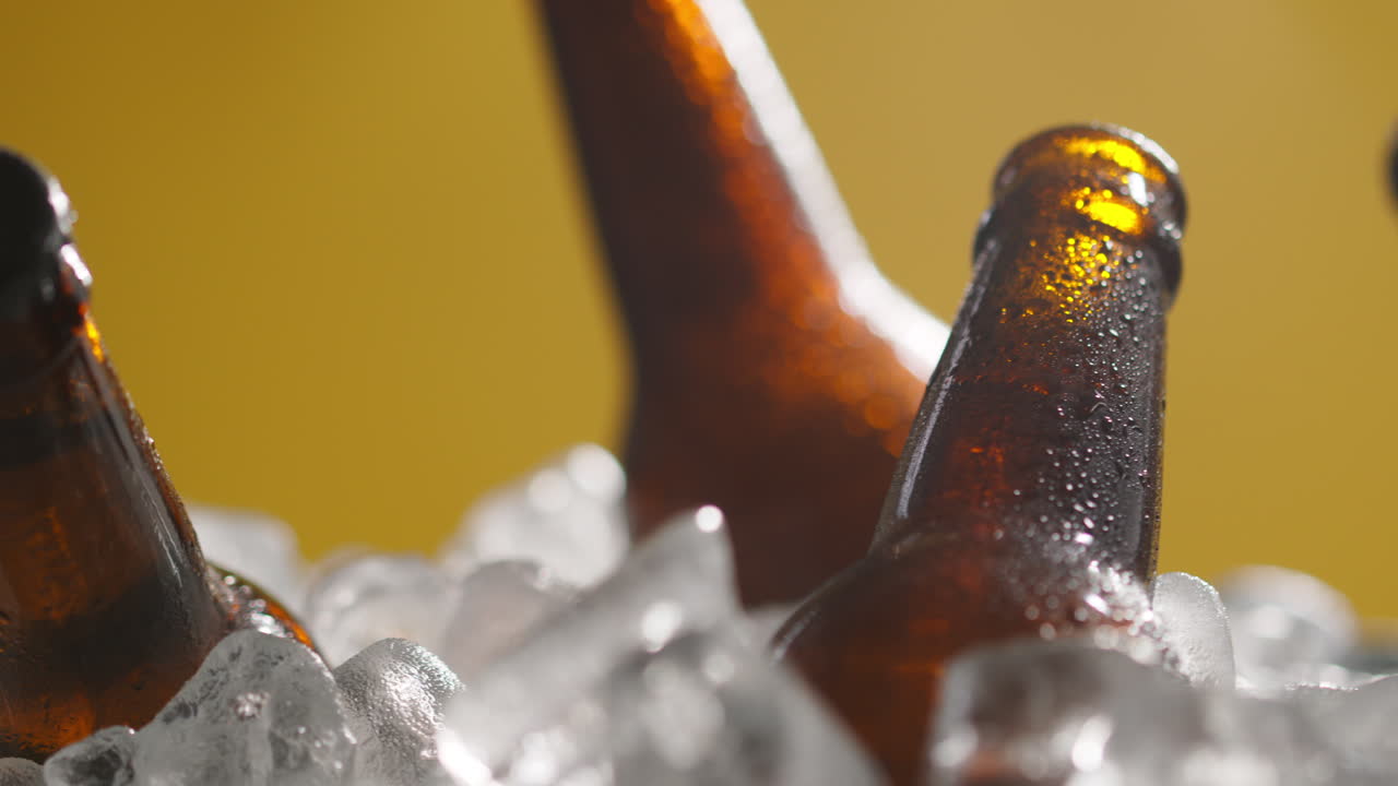 cerrar las botellas de vidrio de cerveza fría o refrescos que se enfrían en un cubo lleno de hielo contra un fondo amarillo