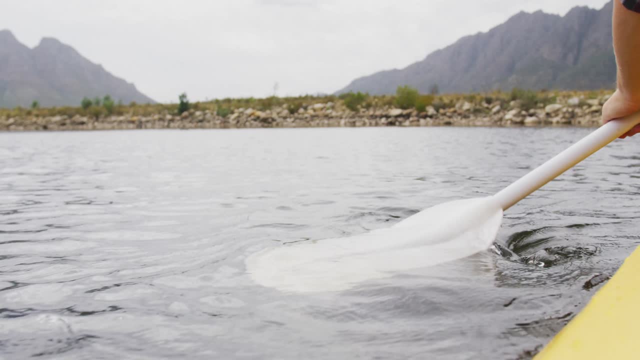 hombre caucásico pasando un buen rato en un viaje a las montañas, en kayak en un lago, sosteniendo un remo