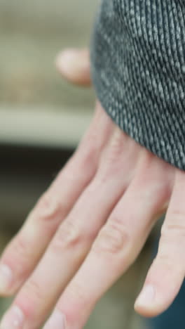 una vista de cerca de la mano de un hombre con una chaqueta de traje gris y pantalones vaqueros azules, caminando a lo largo de las vías del ferrocarril, sosteniendo un puño y liberando su mano