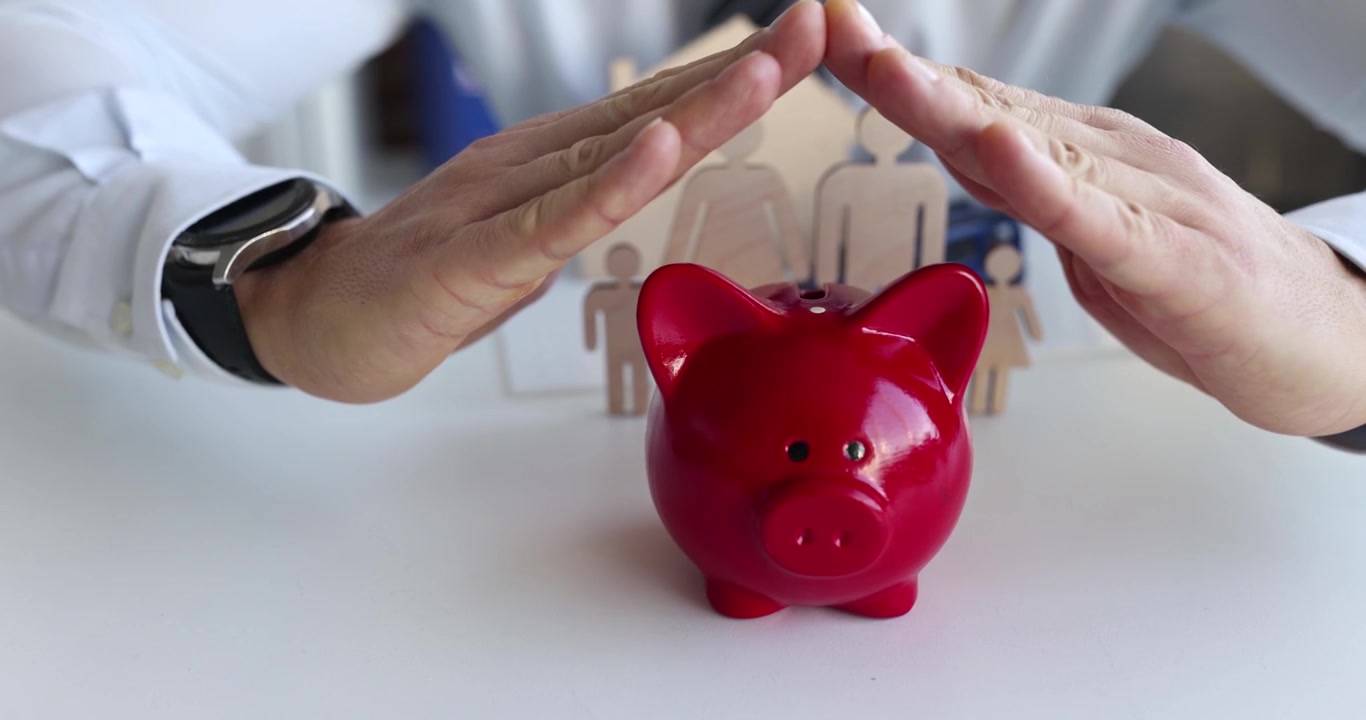 Man creates protective gesture over piggy bank and figurines