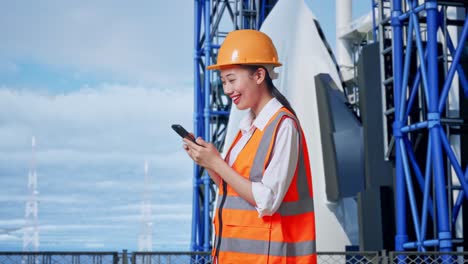 vista lateral de una ingeniera asiática con casco de seguridad usando un teléfono inteligente mientras está de pie con el transbordador espacial