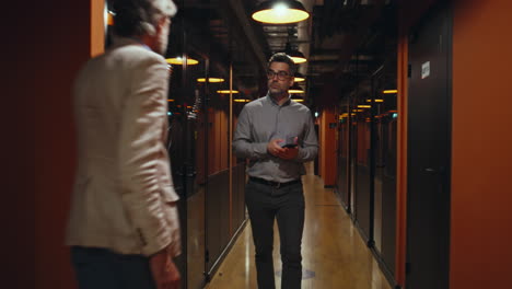 man walks and uses phone in modern office corridor, passing a colleague