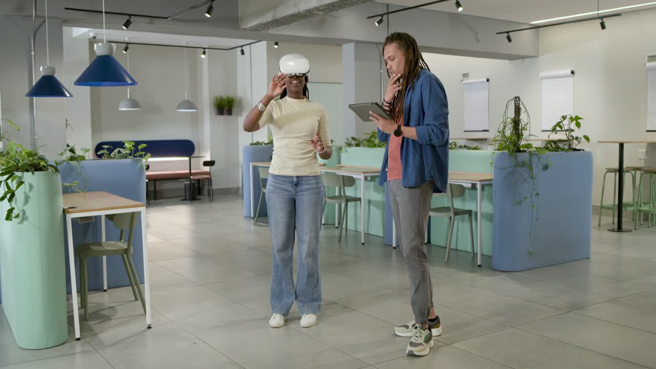 Afroamerikanske kolleger, mann trykker på nettbrett og veileder kvinne med hvit VR-brille som bruker VR-app