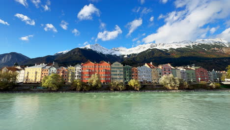 Innsbruck-Austria-colorful-pastel-buildings-capital-Tyrol-Tyrolean-Alps-mountain-backdrop-the-bridge-over-the-Inn-River-cars-bikes-people-sunny-blue-sky-clouds-October-November-autumn-fall-wide-static