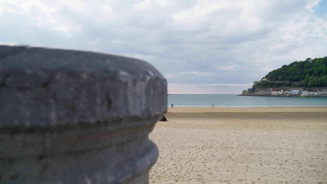 Wide view dolly right of the bay mouth, framed by a stone pillar, hills, and an island