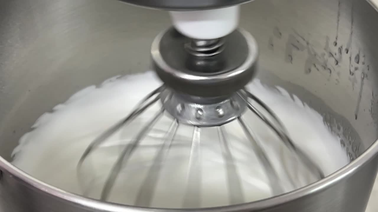 entorno de cocina comercial primer plano de una batidora eléctrica que mezcla clara de huevo y azúcar hasta que es un pico brillante y un pico rígido, preparando crema de mantequilla de merengue