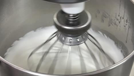 commercial kitchen setting close up shot of an electric mixer mixing egg white and sugar until it is glossy peak and stiff peak, preparing meringue buttercream