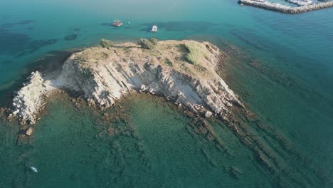 Aerial-of-luxury-sail-boat-yacht-moored-in-open-wide-sea-ocean-water-close-to-a-little-rocky-islet-exploring-snorkelling-and-diving