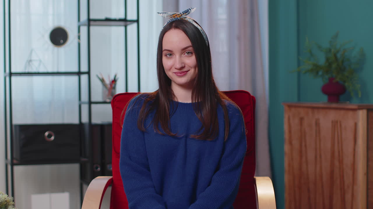 mujer joven sonriendo amistosamente a la cámara, agitando las manos gestando hola, hola, saludando en casa en la silla