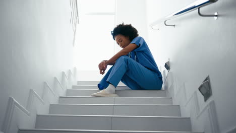 stressed and tired female nurse wearing scrubs sitting on stairs in hospital