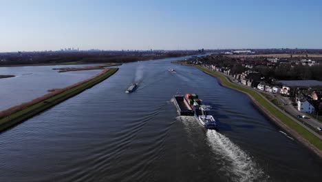 vehículos que circulan por la carretera ribereña con barcazas que navegan en el río noord cerca de hendrik-ido-ambacht, países bajos