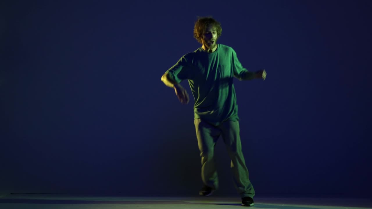 Stylish young man, hip-hop dancer dancing isolated over dark blue background in neon light. Modern dance art, fashion, youth, ad, style. 4K, video