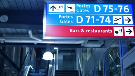 señal de puertas en un aeropuerto, con un hombre subiendo las escaleras mecánicas en el fondo