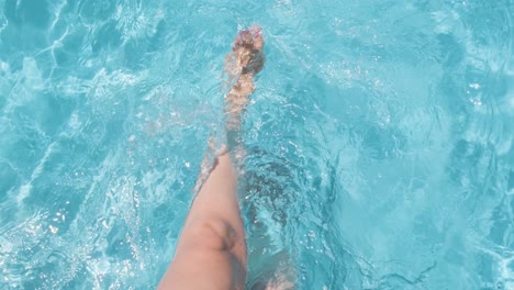 female sitting on poolside, splashing water with legs, clear crystal water in slow motion