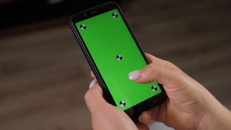 un primer plano de la mano de una mujer navegando por un teléfono inteligente con pantalla verde en casa.