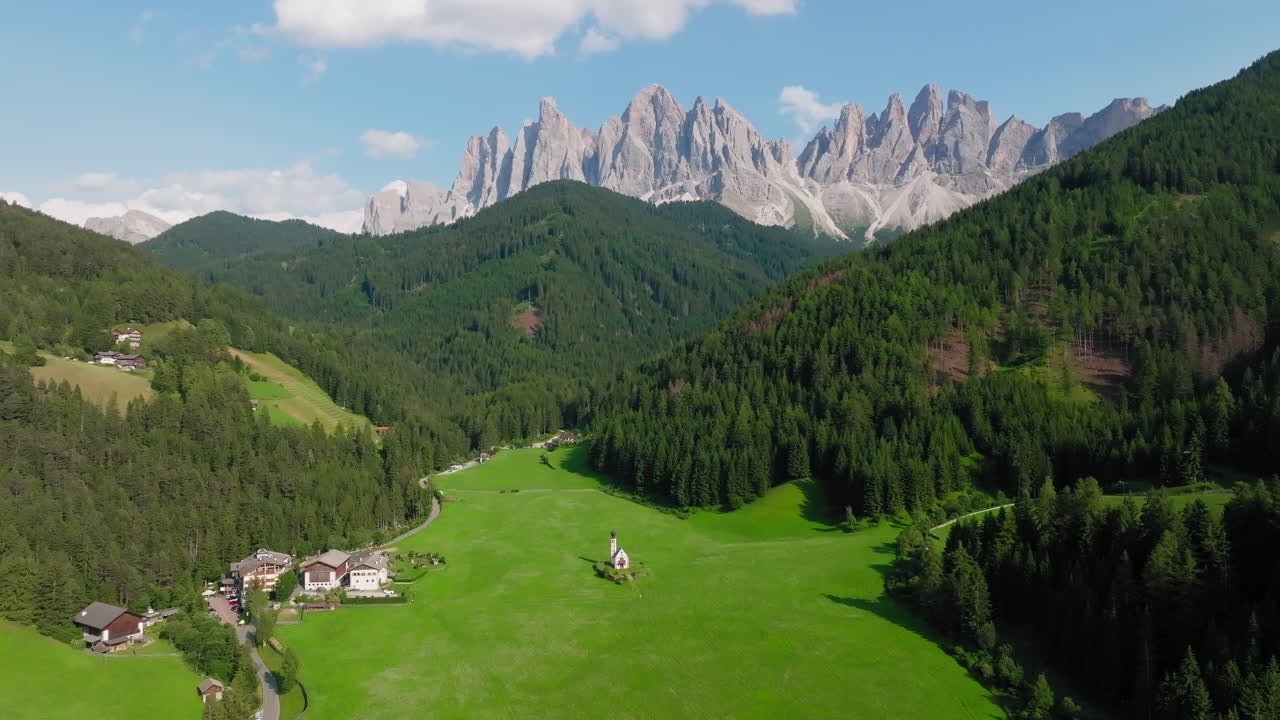 Slow panning drone shot of Church of St. John in Val Di Funes, Ranui, Italy, during springtime. Odle mountains in the background