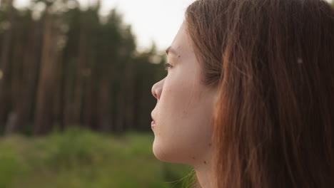 lady stands in heart of forest at sunset. young woman looks confused thinking about personal problems in evening. pastime in nature to get rid of stress