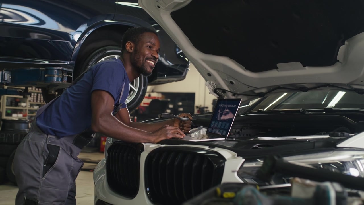 Meccanico afroamericano in un'officina moderna che esegue la manutenzione del veicolo con il cofano aperto.
