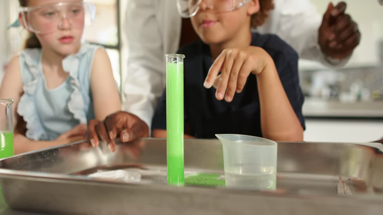 Teens in goggles at lab, teacher guiding student adding tablet into cylinder, forming green foam