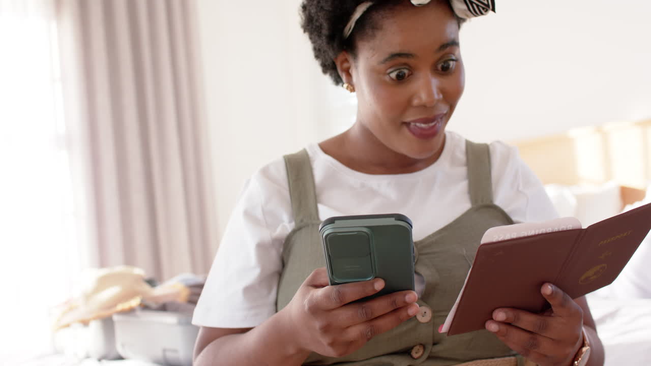 African American woman holds a passport and travel gadget at home, booking a vacation