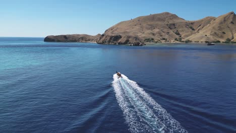 drone following and descending over a speedboat racing towards a dry and barren island