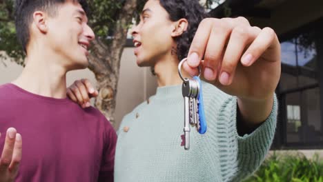 happy diverse male moving house, holding keys, embracing and smiling