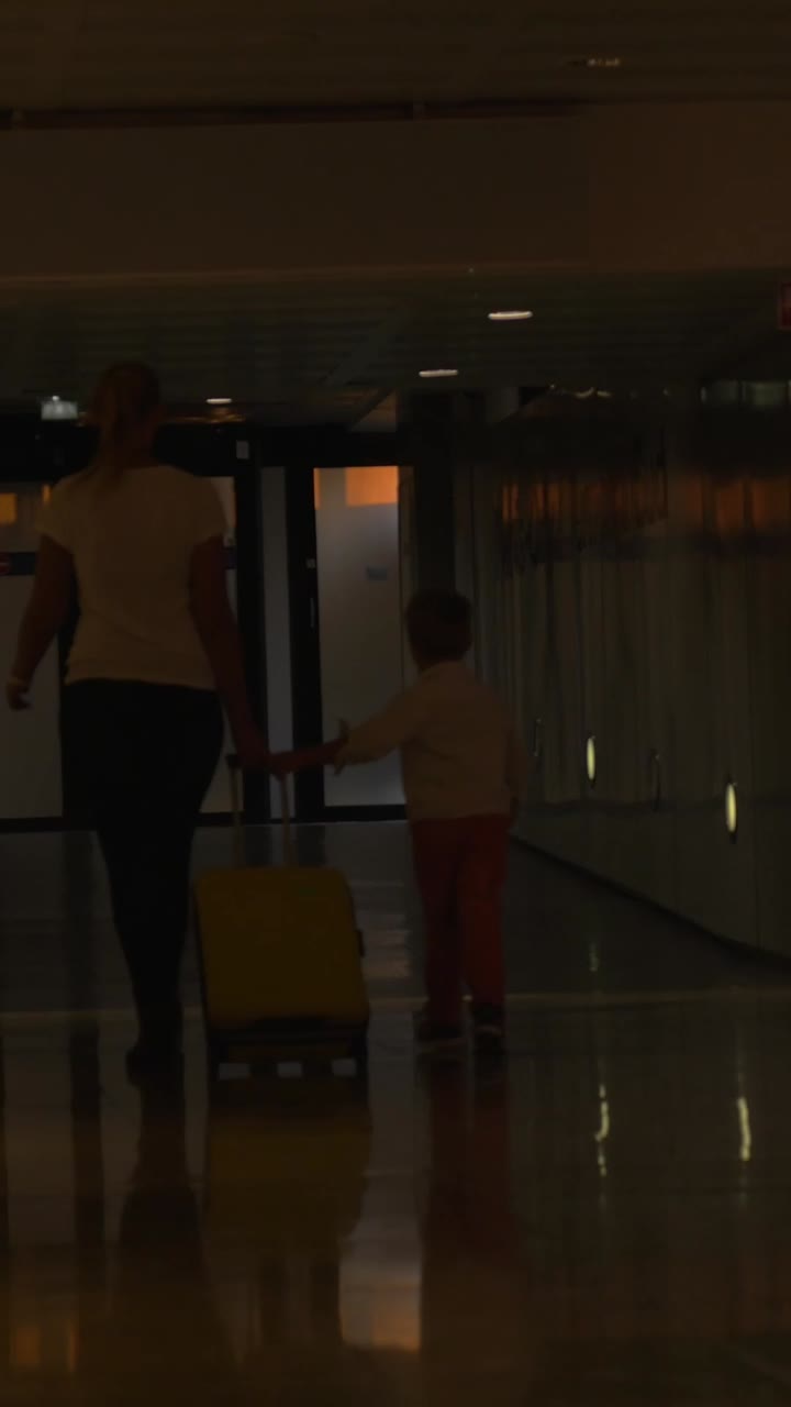 Mujer y niño caminando con una maleta amarilla en la terminal del aeropuerto