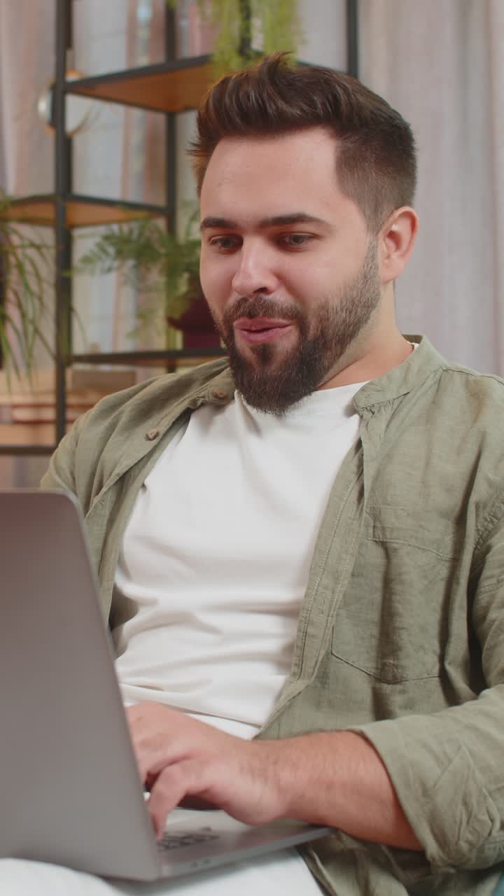 Surprised caucasian brunette man using laptop computer sitting on sofa couch at home apartment